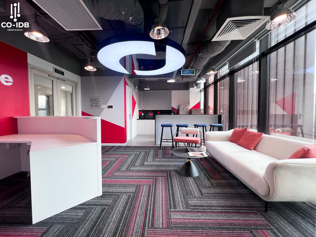 Thiết kế văn phòng với layout mở, tông xám – đỏ nổi bật, ghế bar hiện đại, sàn thảm họa tiết cá tính và hệ trần lộ kỹ thuật mang tinh thần năng động, sáng tạo.