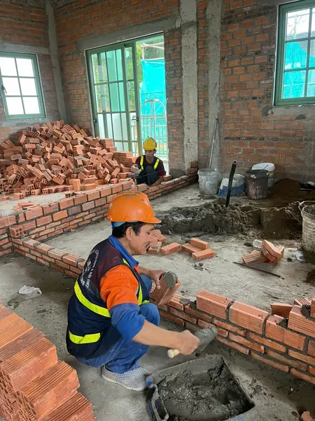 Hình ảnh các công nhân xây dựng đang tập trung thực hiện công đoạn xây tường gạch, thể hiện sự chính xác và tỉ mỉ trong từng đường xây, đảm bảo cấu trúc vững chắc cho không gian nội thất của dự án.