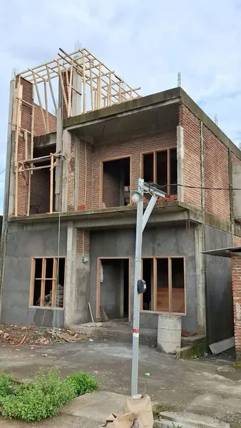 Hình ảnh một ngôi nhà đang trong quá trình hoàn thiện phần thô, bao gồm khung mái gỗ, tường gạch trần và các khung cửa sổ đã được lắp đặt, thể hiện tiến độ xây dựng thực tế.