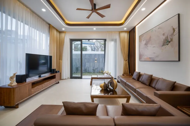 Không gian phòng khách nhà cấp 4 ấm cúng với hệ trần gỗ tự nhiên sang trọng, bộ sofa gỗ đệm da cao cấp, bàn trà đồng bộ và khung cửa sổ đón ánh sáng tự nhiên.