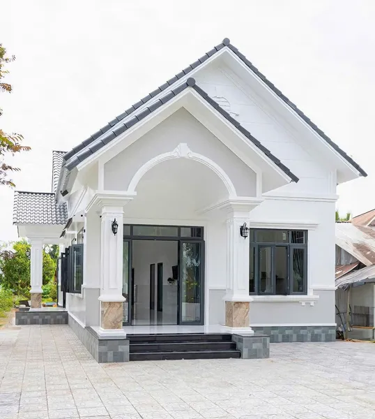 Mẫu nhà cấp 4 mái thái hiện đại màu trắng xám, có vòm cuốn sảnh chính, cột vuông kiên cố và hệ cửa nhôm kính đen.