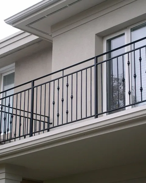 Góc ban công của ngôi nhà với lan can sắt sơn đen gồm các thanh dọc thẳng đứng đan xen các con tiện tròn trang trí tinh tế, nổi bật trên nền tường màu sáng.